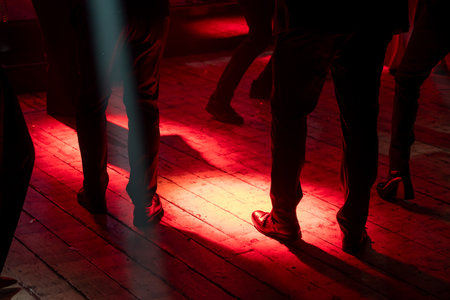 Feet of people dancing on wooden floor illuminated by vibrant red lights, creating energetic party atmosphere.の写真素材