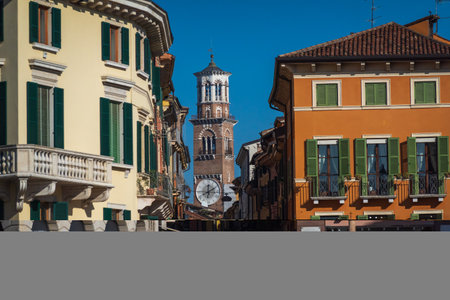 Street view in Verona with vibrant buildings and ancient clock tower under blue sky. Captures architectural charm and history in Italy.の写真素材