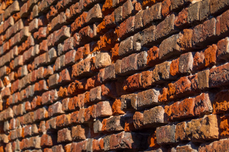 Detailed view of rugged red brick wall showing unique texture and warm tones. Natural light highlights the intricate surface, creating an impression of depth and character in architectural design.の写真素材