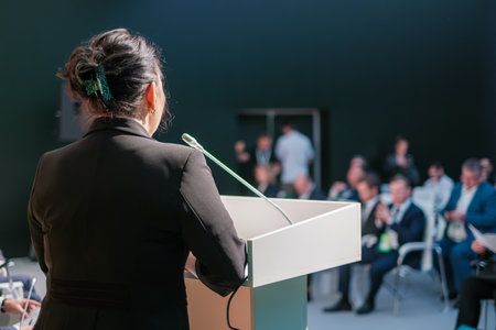 Professional speaker addressing an audience at a business conference in a formal setting.の写真素材