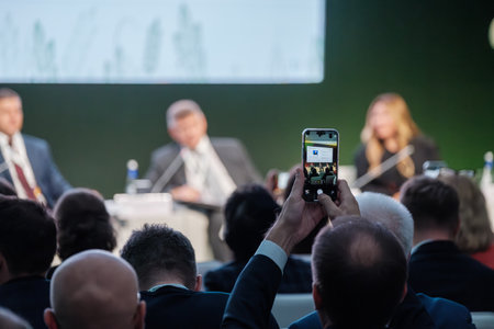Audience member photographs conference speakers on stage at corporate presentation event using phoneの写真素材