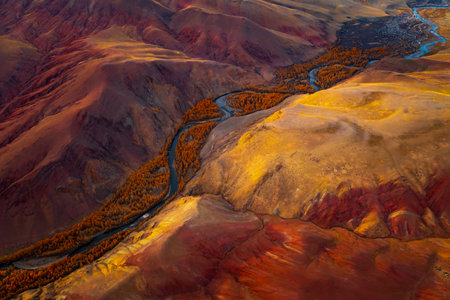 Aerial perspective of a vibrant red and orange rugged valley with a meandering river, featuring dramatic erosion patterns and enhancing the majestic Altai Mountains landscape.の写真素材