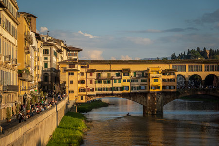 Golden sunlight bathes Florences historic Ponte Vecchio and vibrant riverside area along the Arno River.の写真素材
