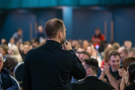 Professional presenter giving speech in crowded venue showcasing communication and engagement skills during eventの写真素材