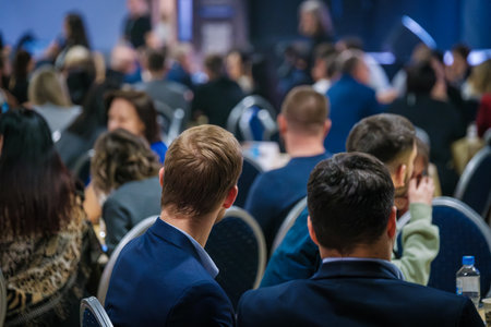 Professionally dressed individuals attending a conference in a formal setting with blue chairs.の写真素材