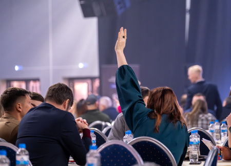 Conference attendee raising hand in crowded hall, illustrating education, participation, and engagement.の写真素材