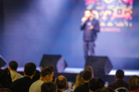 Blurry speaker on stage with an audience seated and focused on the eventの写真素材