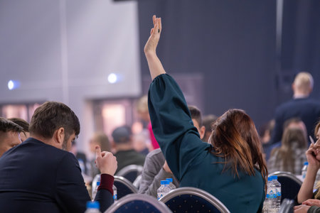 Audience member raising hand at an event panel discussion involving active participation.の写真素材