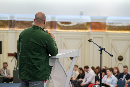 Speaker engages audience in conference room setting with microphone and podium backdrop.の写真素材