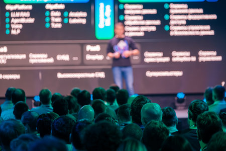 Blurry man giving presentation to interested attendees during corporate business conference in large...