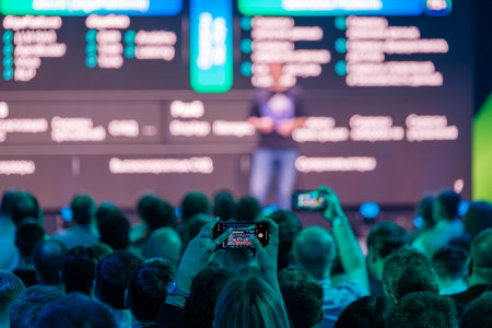 Crowd attending presentation while capturing moments on smartphones, highlighting modern event...