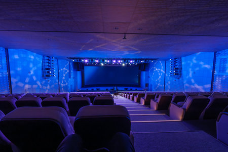 Modern theater interior with blue illumination, rows of seats, and performance-ready stage lighting.