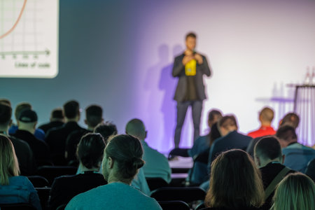 Business professional speaks at event with audience sitting attentively during presentation in hall