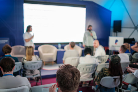 Business seminar scene with attendees paying attention to speaker in a modern conference setting.