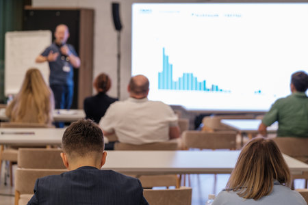 Participants watching a presentation in conference setting focused on speaker and visual data