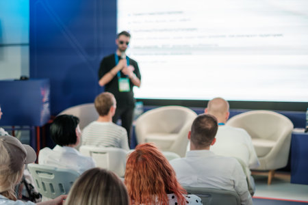 Speaker discussing topics in front of audience during conference. Audience attentively listening to...