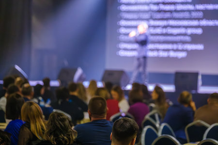 Speaker presenting at conference to engaged audience in dimly lit auditorium with stage lighting.の写真素材