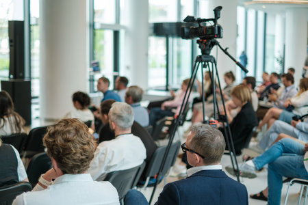 Business seminar with engaged audience in modern bright venue, with professional camera setup.の写真素材