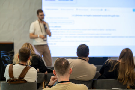 Group of attendees observing speaker delivering presentation in a seminar setting with projector