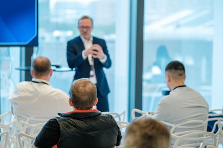 Business professional giving presentation to engaged audience in modern conference setting with...