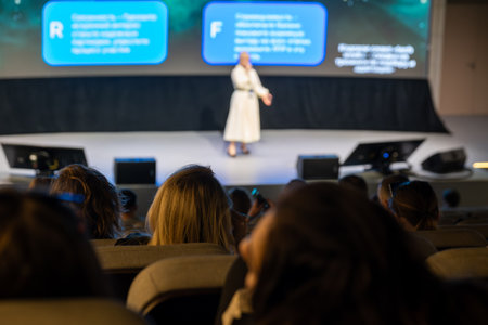 Speaker in white presenting at conference with audience watching from seating areaの写真素材