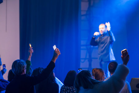 Man sings on stage illuminated by blue light while audience holds lighters and phones highの写真素材