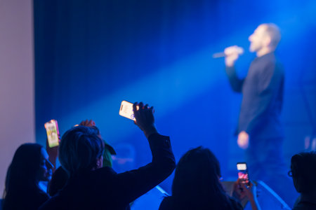 Concert crowd capturing vibrant performance on stage with mobile phones in hand under lightsの写真素材