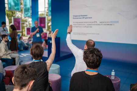 Audience raises hands during conference session with speaker on blue stage and large screen