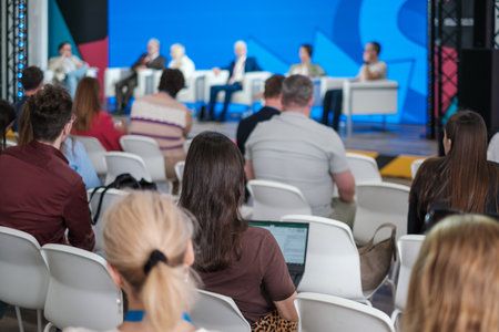 Panel discussion at modern conference featuring diverse speakers addressing audience against bright...