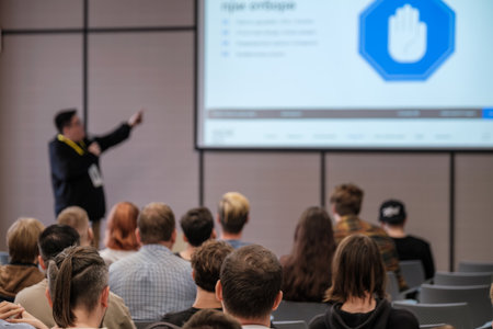 Presenter speaks to attentive audience during conference while large screen shows slides and blue shield iconの写真素材