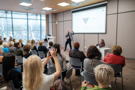 Presenter talks to attentive audience during conference in bright modern room with projector screen and panel at frontの写真素材