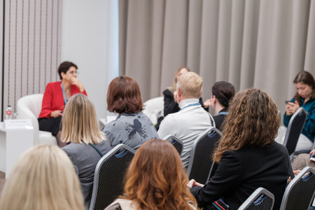 Panel discussion with business professionals in conference room audience listening to speaker wearing red jacketの写真素材