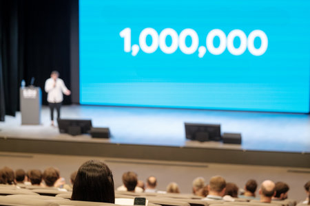 Blurred conference hall stage speaker and huge blue screen reading 1,000,000 audience watches intentlyの写真素材
