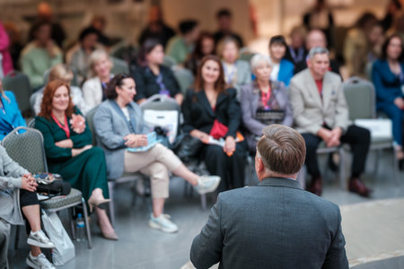 Speaker facing audience of professionals at conference, audience attentively listening, diverse group in business attire, collaborative learning, professional event atmosphereの写真素材