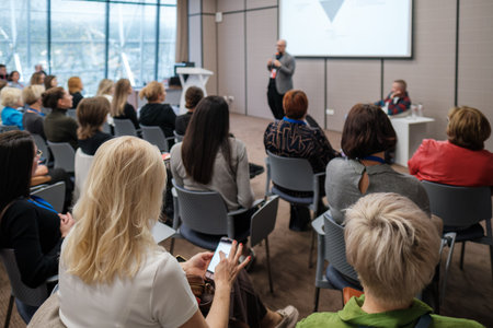 Audience in conference room listens to speaker presenting on screen diverse professionals attend workshop, showing focus and engagement during presentation and discussion in modern corporate setting.の写真素材