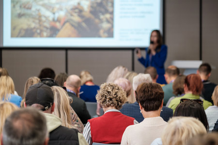 Audience in conference room watches speaker presenting slides on large screen during business eventの写真素材