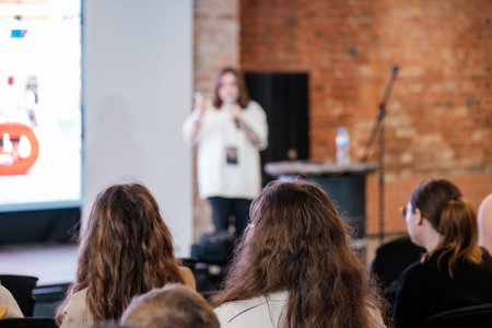 Audience watches blurred speaker presenting on stage in brick wall room during conference style eventの写真素材