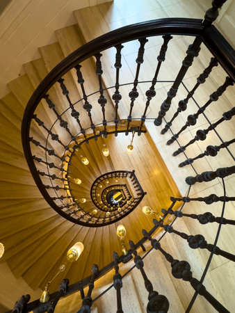Spiral staircase from above featuring dark iron balusters and glowing pendant lights creating...