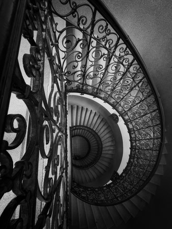 Black and white spiral staircase reveals ornate wrought iron railing curved design depth perspective...