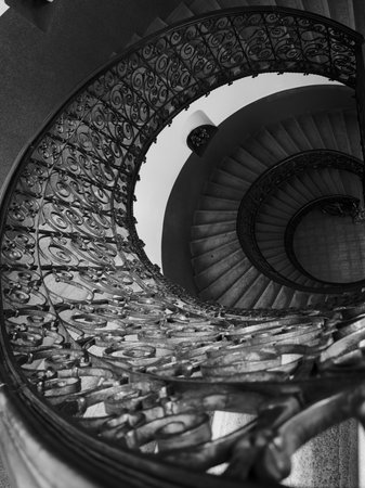 Monochrome spiral staircase overhead view shows decorative iron railing winding steps creating dramatic depth and symmetryの写真素材