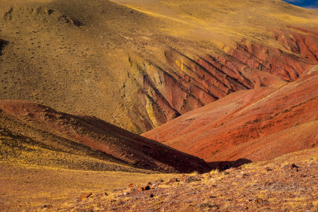 Vibrant desert hills in warm yellows oranges reds with jagged ridges and sparse vegetation dramatic...
