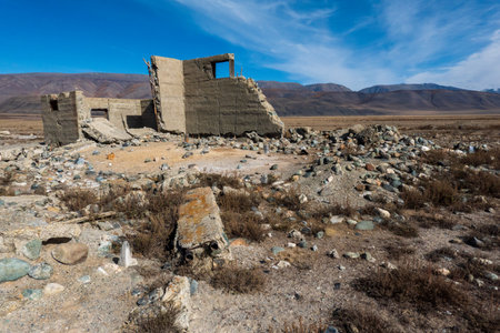 Abandoned concrete building ruins in desolate desert setting with rocky terrain and mountains.の写真素材