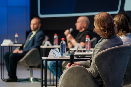 Panel discussion at conference features speakers seated in soft chairs microphones on table water bottles name cards. Professional focused atmosphere fosters collaboration learning inspirationの写真素材