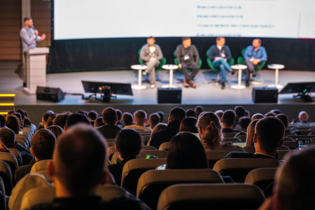 Panel of five speakers on stage during conference talk, audience listening intently in theater settingの写真素材