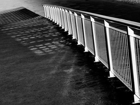 Black and white image features metal railing beside walkway with strong diagonal lines and patterned...