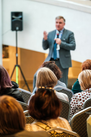Speaker in suit delivers presentation to attentive audience at conference sharing insights on...