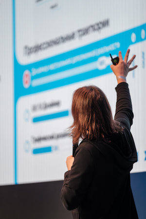 Presenter stands before large screen showcasing charts during conference, pointing with laser...