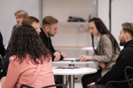 Coworkers sit around round table in bright workspace. They review papers and devices while focused on discussion. Friendly collaborative atmosphere fosters teamwork and planning for upcoming project.の写真素材