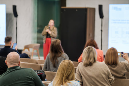 Audience listens to speaker during workshop in bright conference room. Attendees focus on...
