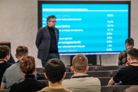 Audience listens to speaker during conference presentation blue screen displays data and charts...